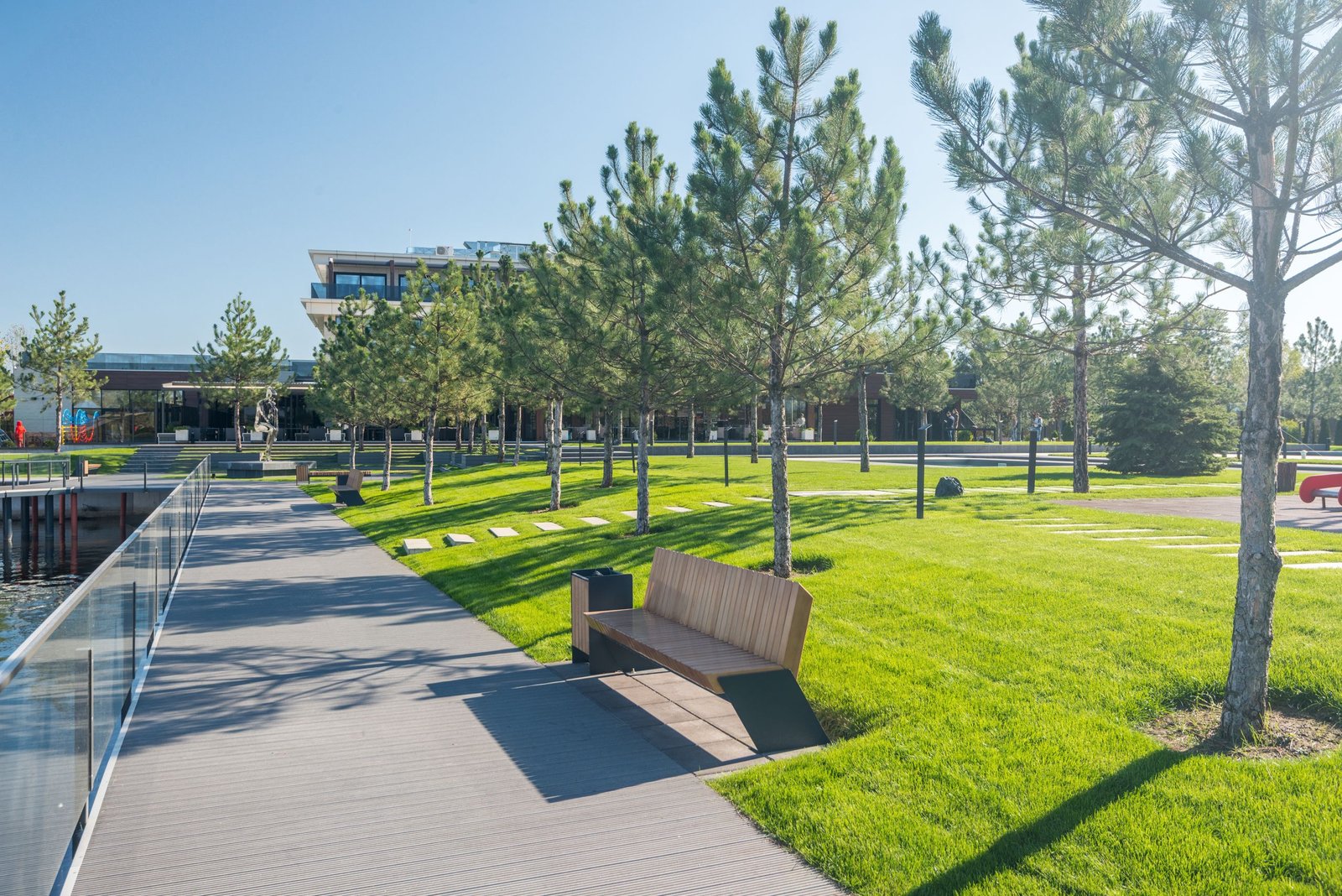 Lawn Mowing A serene view of a sunny park with benches, footpath, and lush greenery.